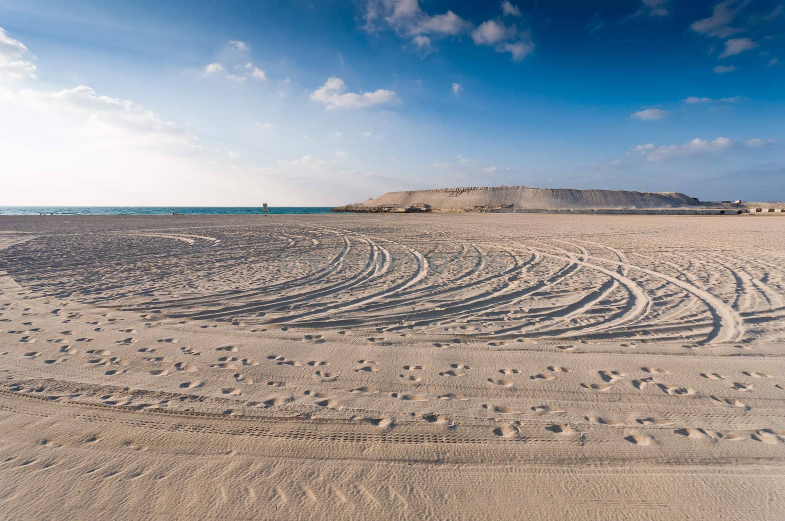 sandy beach with lots of footprints and a blue sky with clouds