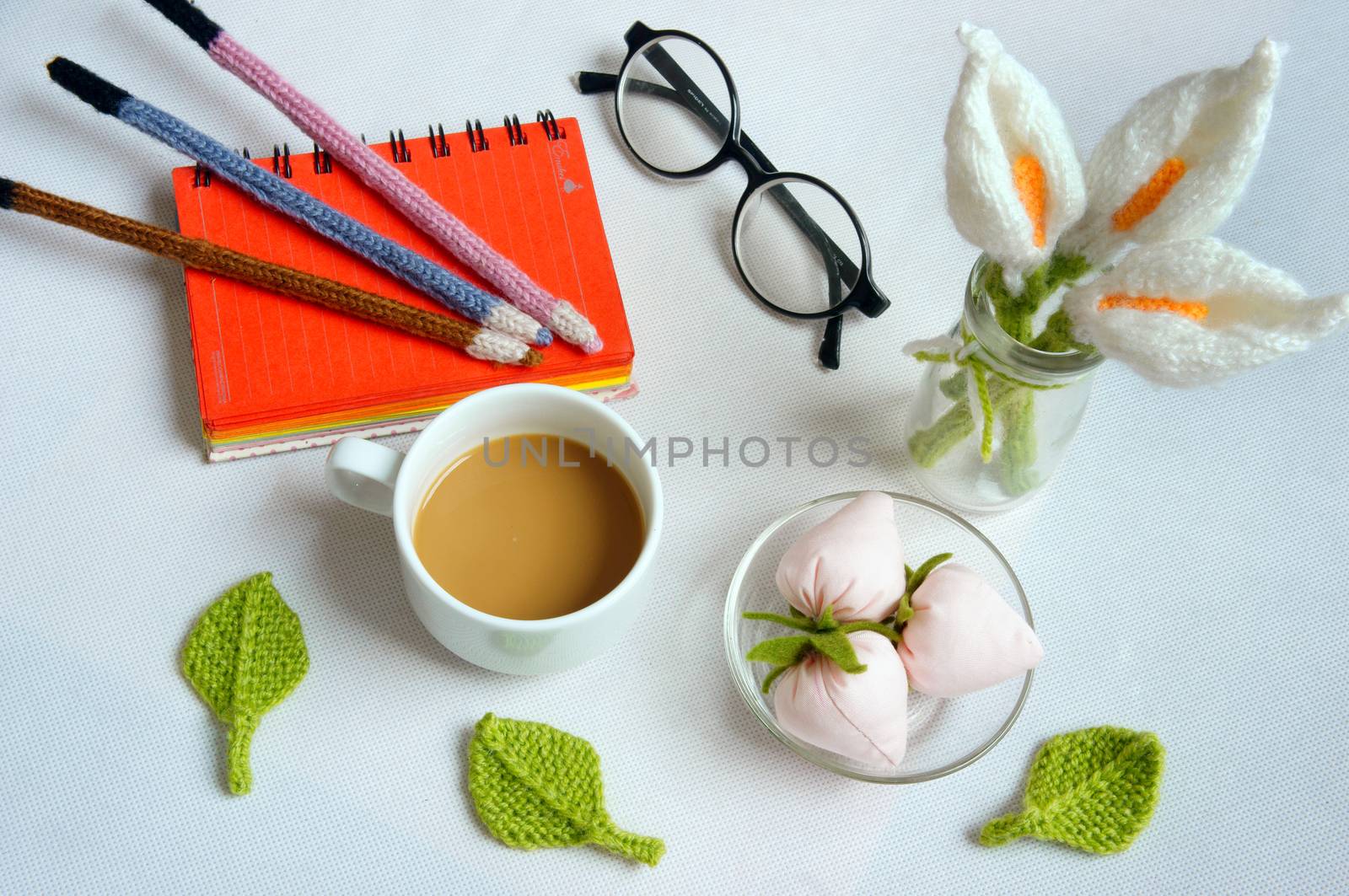 Romantic desk with ornament from handmade product, lily flower knit from white yarn, handbook, knitting pencil, coffee cup, glasses, beautifil craft