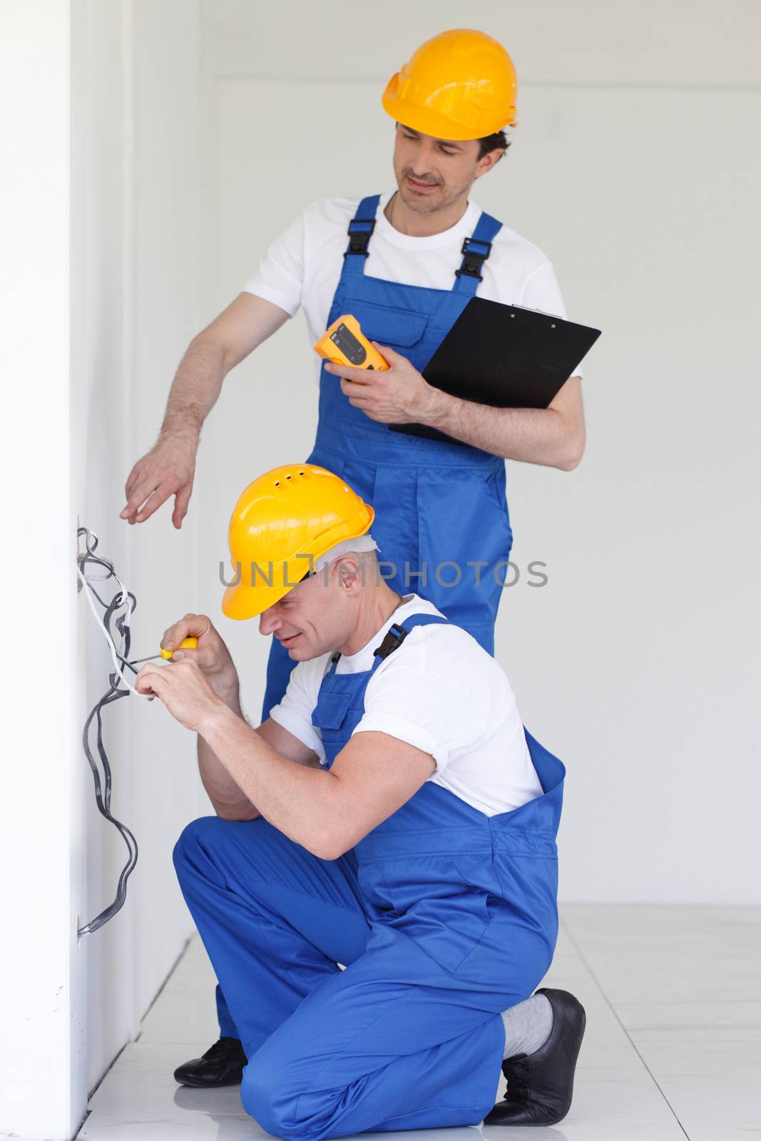 Two builders in helmets working with electricity indoors