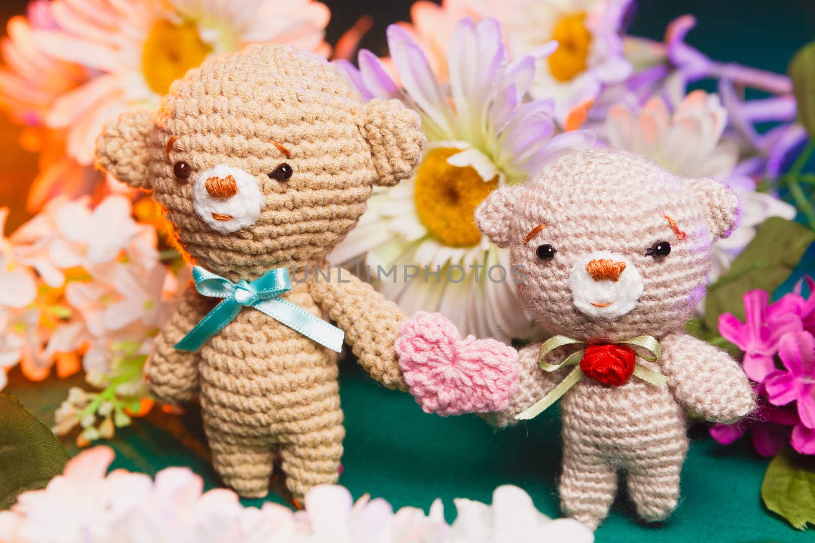 Concept: love, relationship. Couple of knitted bears holding hands with flowers on background