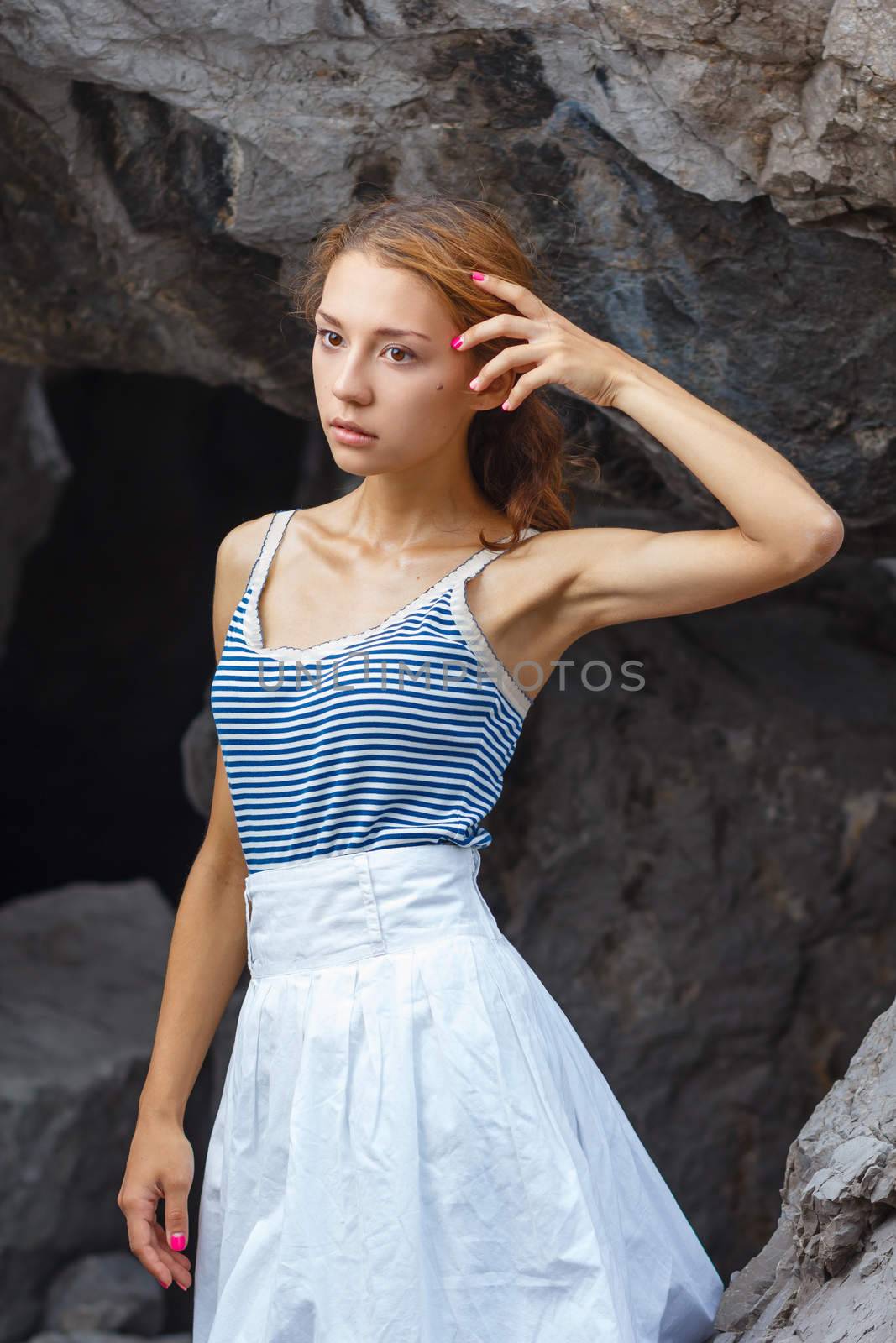 Beautiful young teen girl in dress posing on the stones in the sea fashion shoot at shore