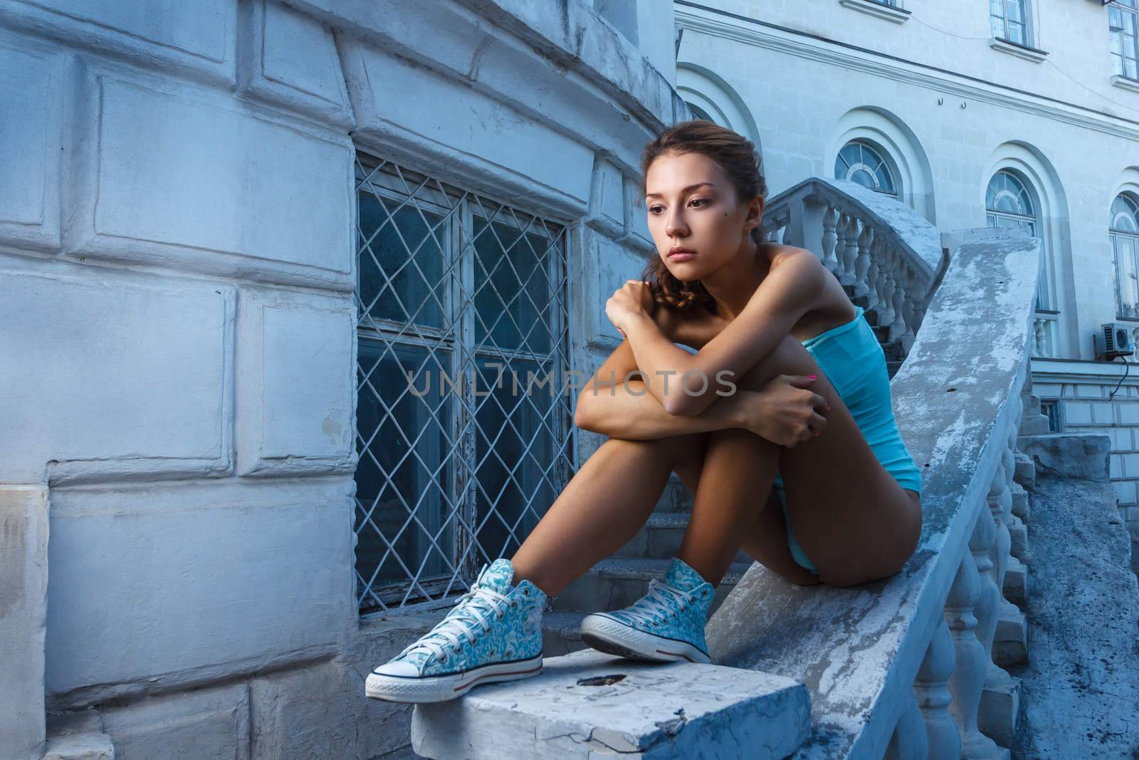 Beautiful young teen girl in bodysuit posing during city fashion shoot with classical building at background