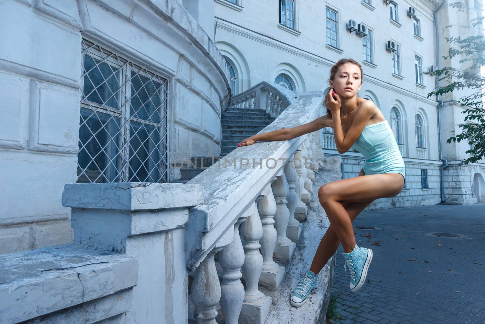 Beautiful young teen girl in bodysuit posing during city fashion shoot with classical building at background