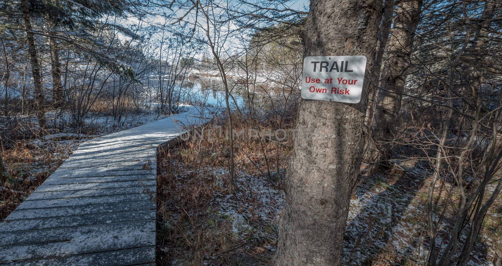 A walking trail warning sign on a tree advises of risk.  Foot path in winter woods. Fresh fallen snow, winter day.