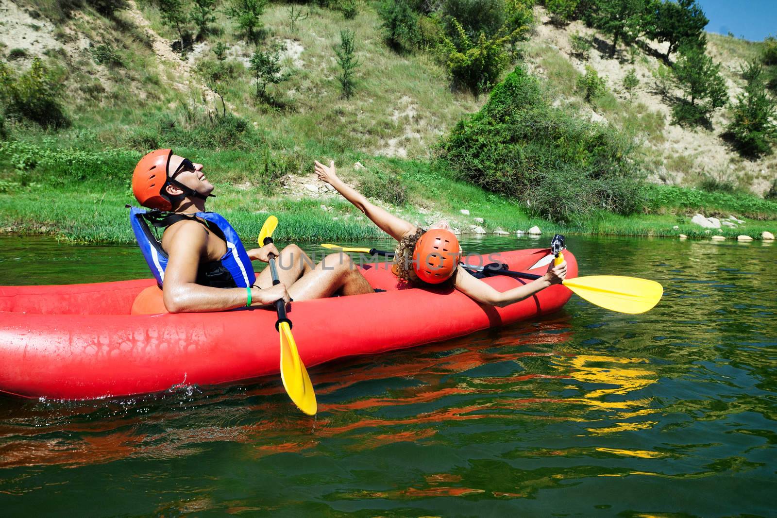 A male and female in a red inflatable canoe celebrating reaching calm waters of a river.