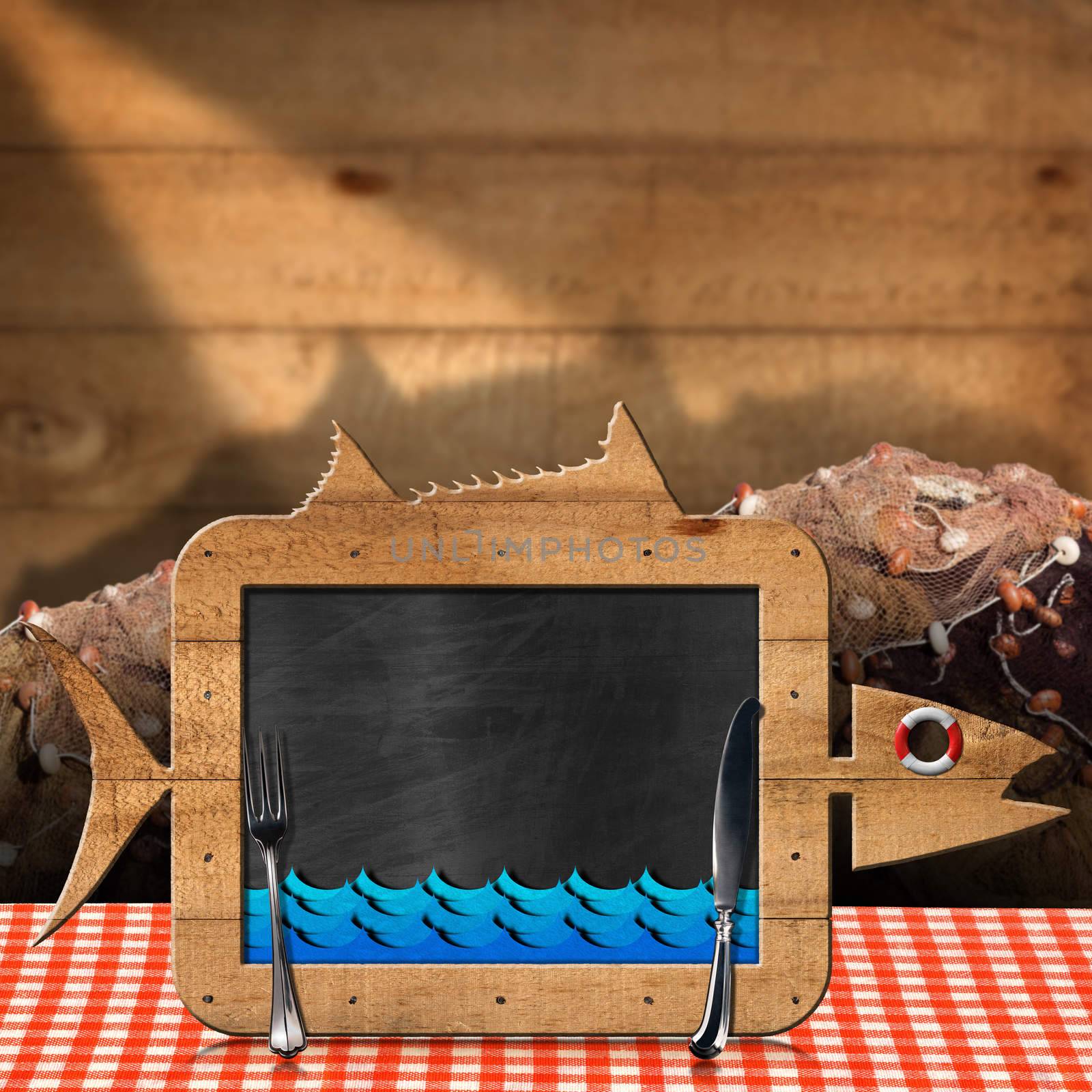 Blackboard in the shape of fish with blue waves and silver cutlery on a table with checkered tablecloth and fishing nets