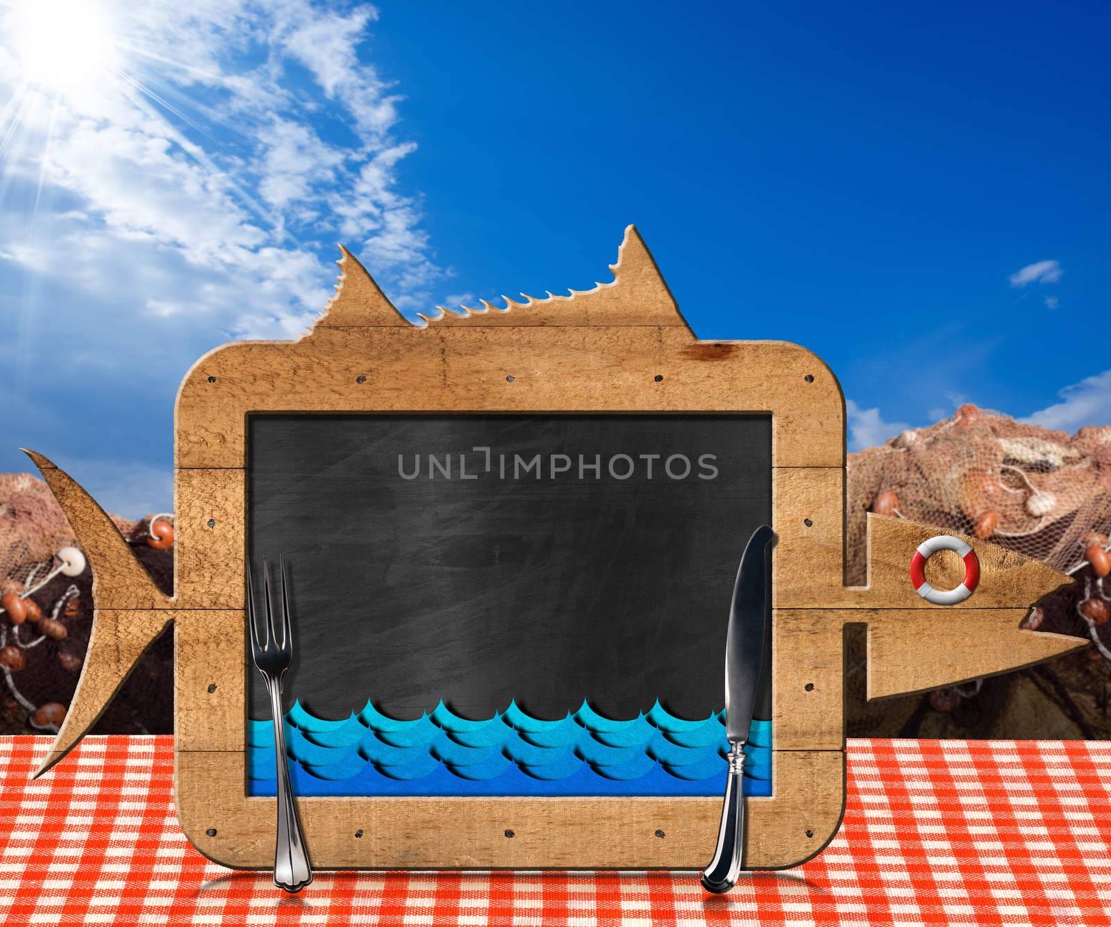 Blackboard in the shape of fish with blue waves and silver cutlery on a table with checkered tablecloth and fishing nets