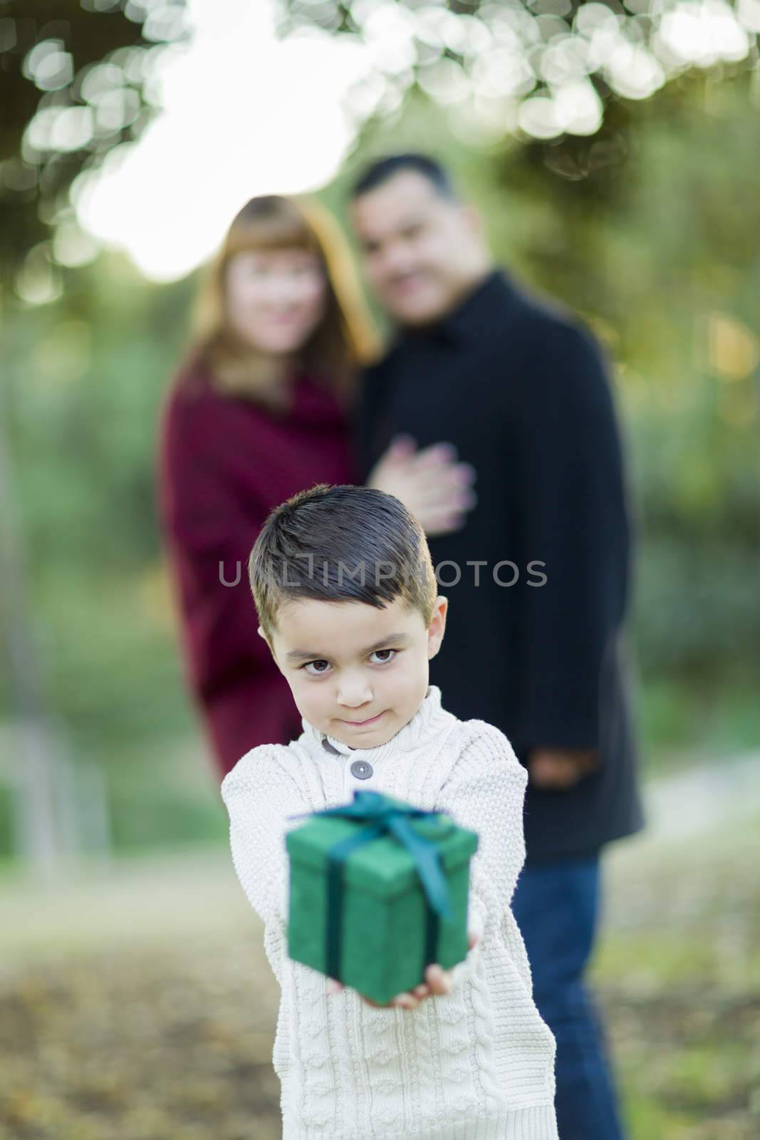 Mixed Race Boy Holding Gift In Front with Parents Behind by Feverpitched