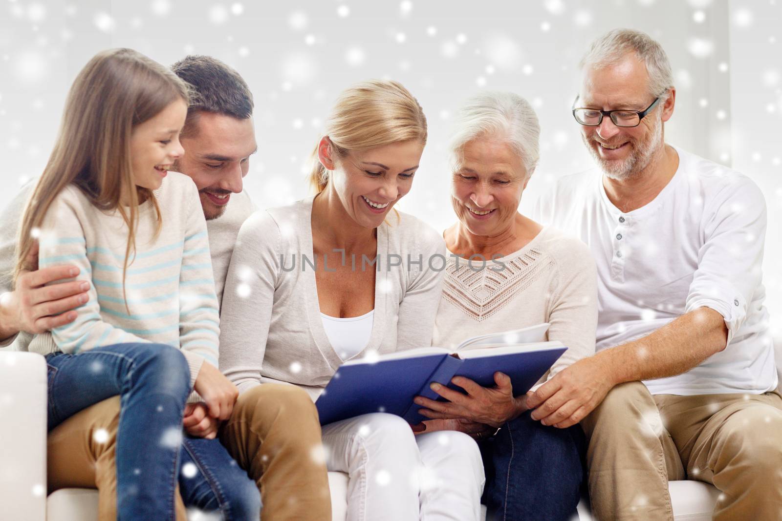 family, happiness, generation and people concept - happy family with book or photo album sitting on couch at home