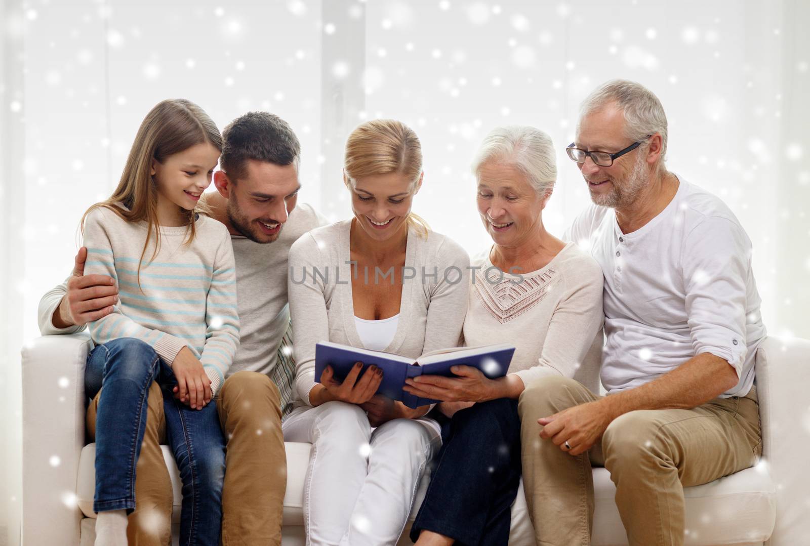 family, happiness, generation and people concept - happy family with book or photo album sitting on couch at home