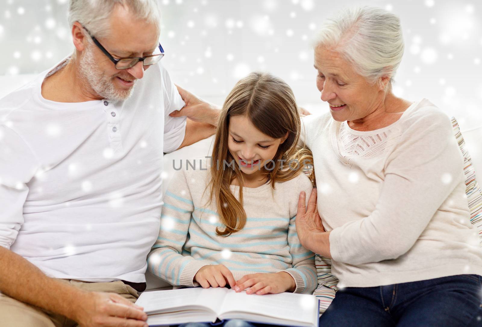 family, generation, education and people concept - smiling grandfather, granddaughter and grandmother with book sitting on couch at home