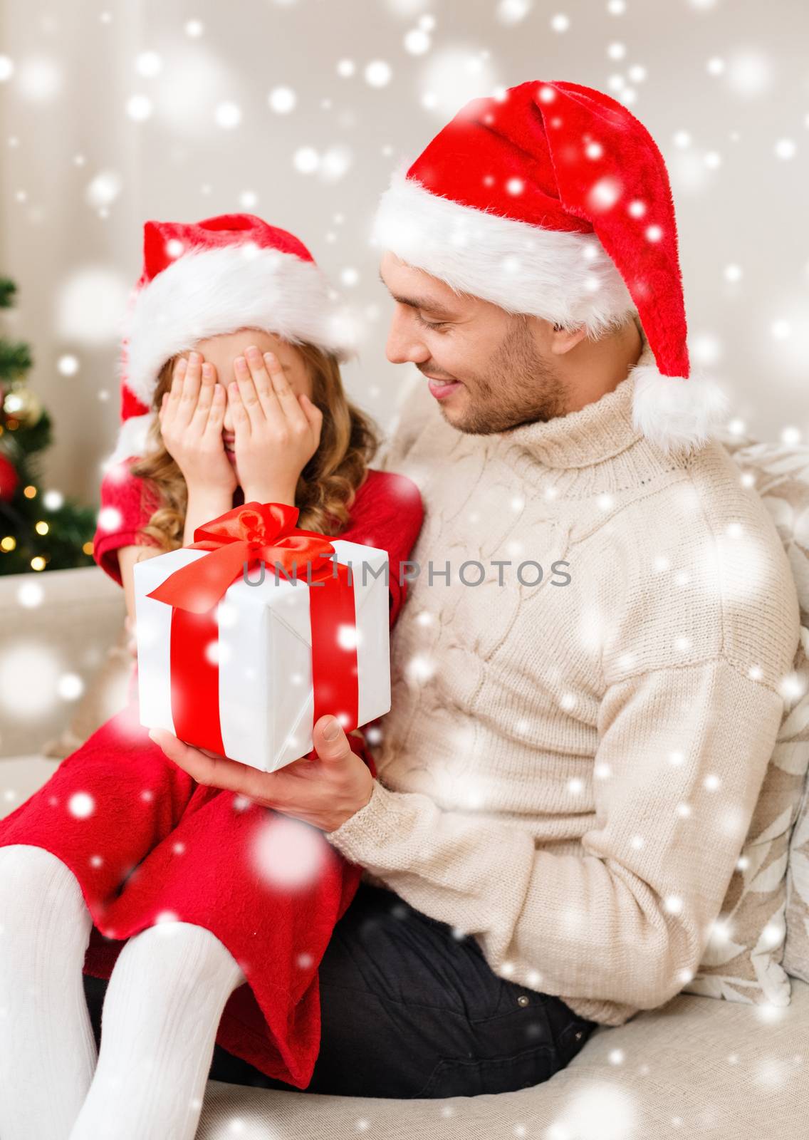 christmas, holidays, family and people concept - smiling father and daughter in santa hats holding gift box and covering eyes at home