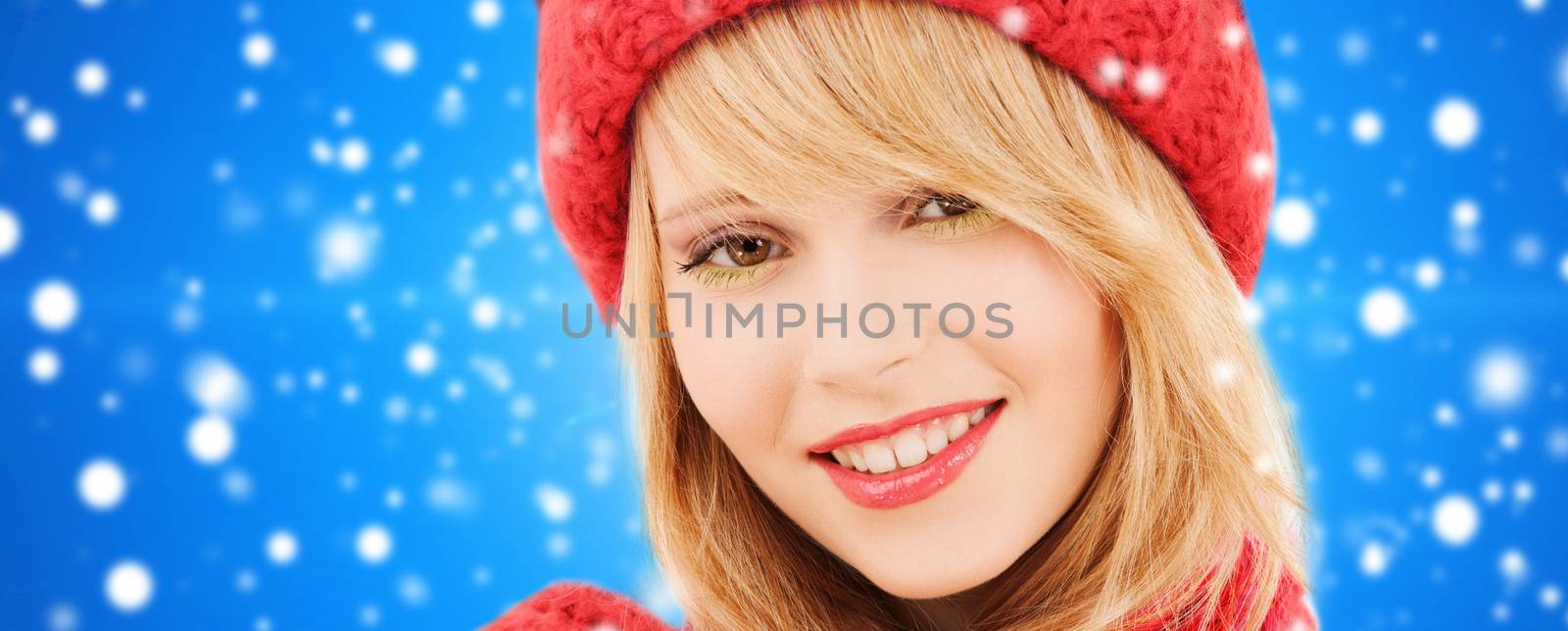 happiness, winter holidays, christmas and people concept - close up of smiling young woman in red hat and scarf over blue snowy background