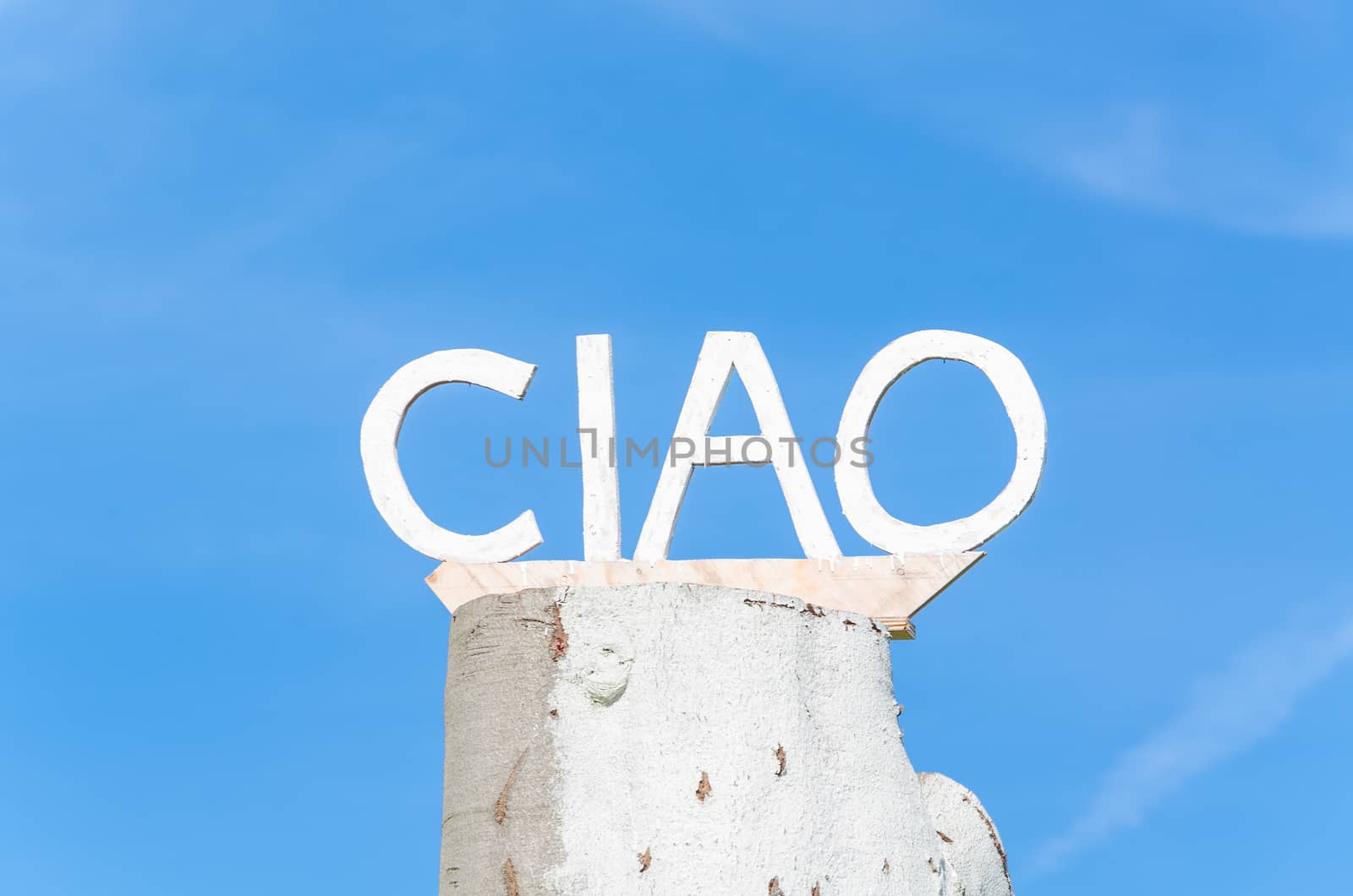 Ciao lettering on an old tree trunk in front of blue sky.