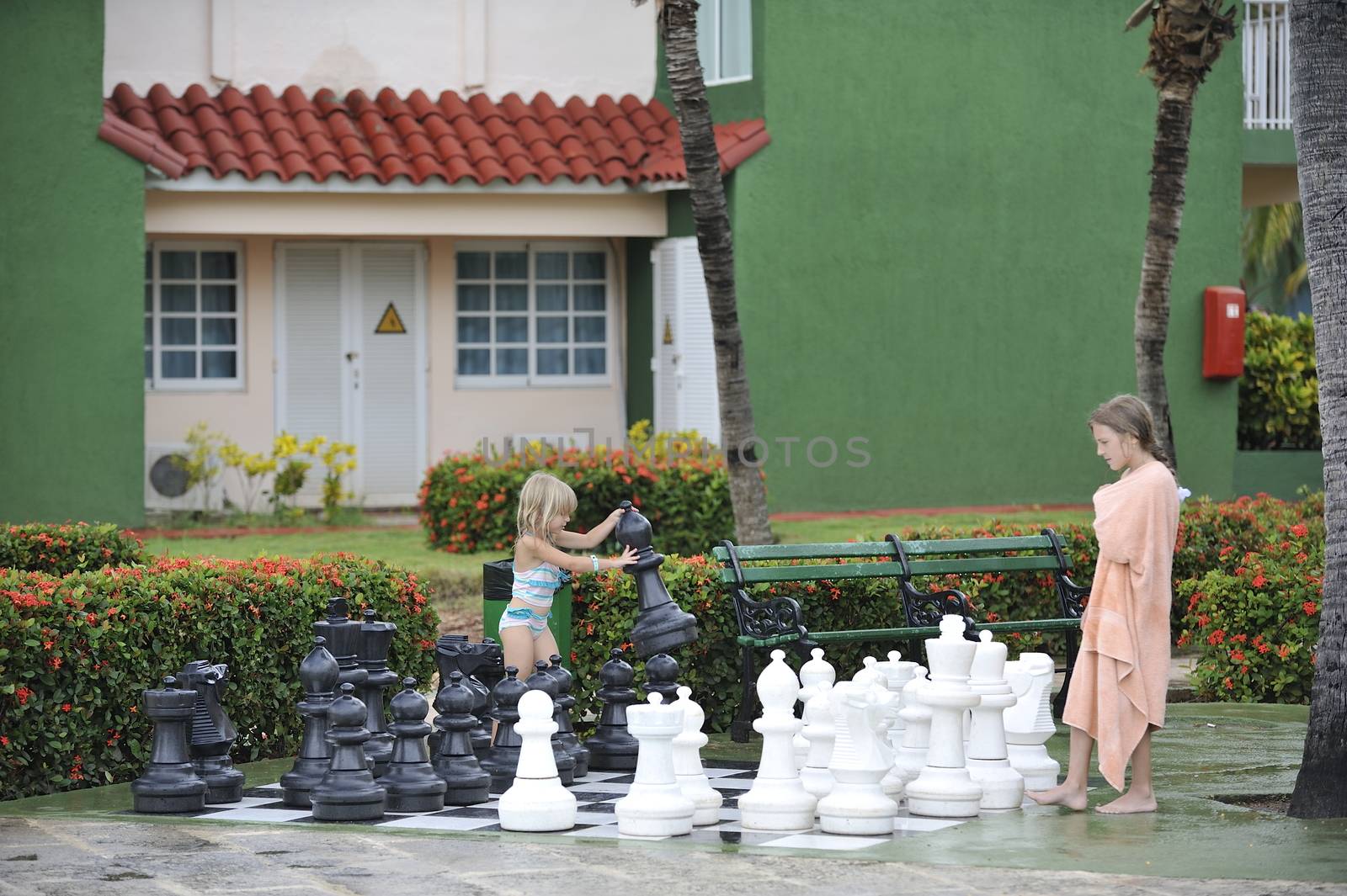 Girls in towels are playing chess with big figures.