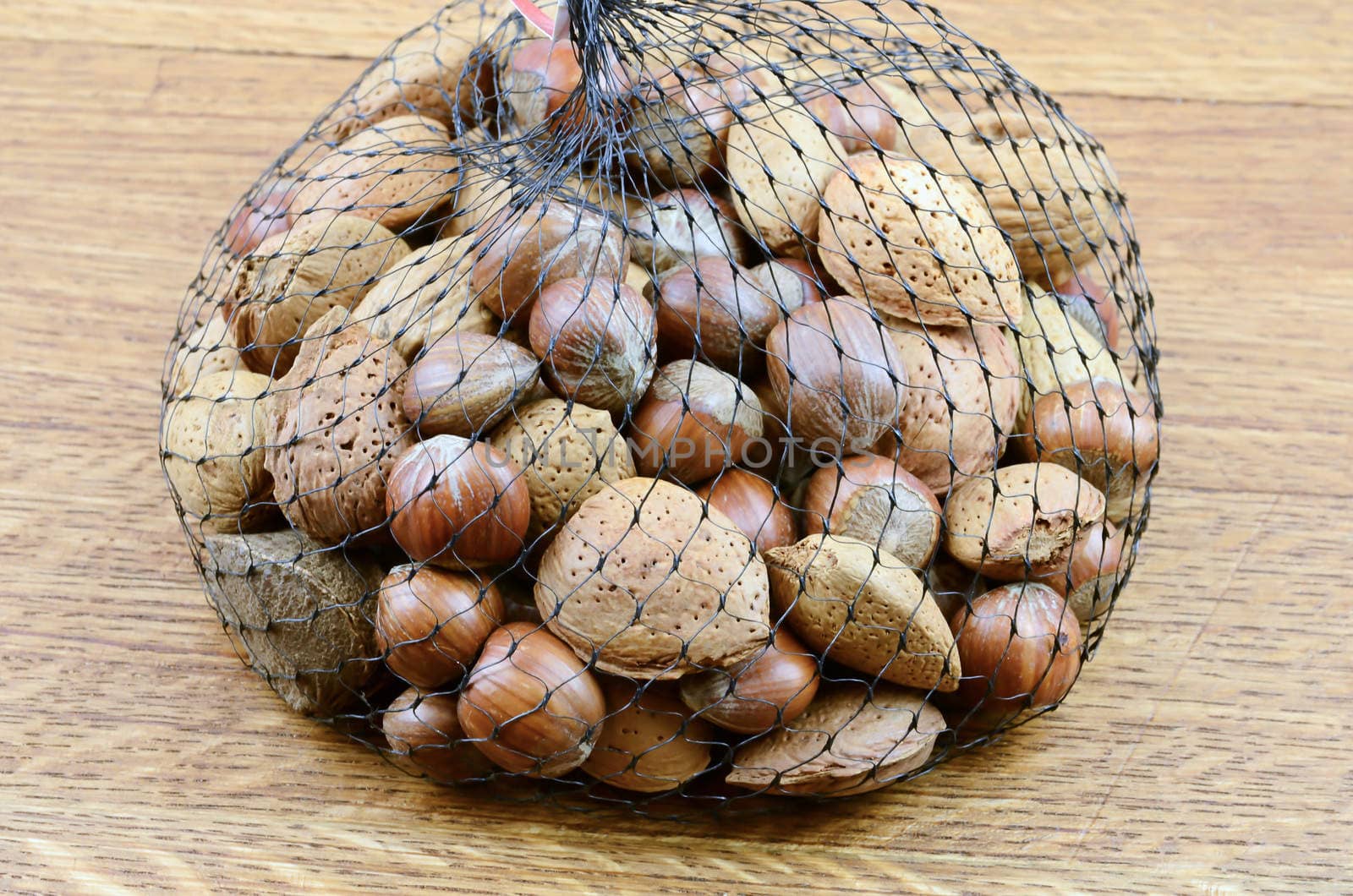 Mixed nuts on wooden background in net sack


