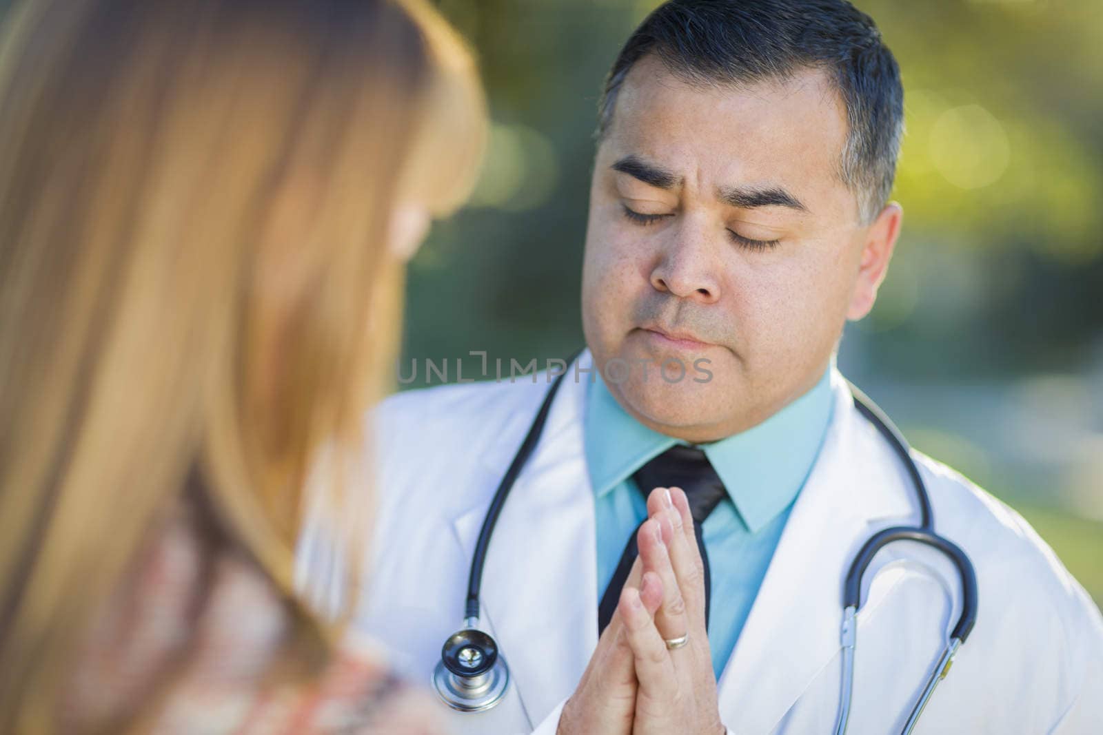 Hispanic Male Doctor Praying With A Patient by Feverpitched