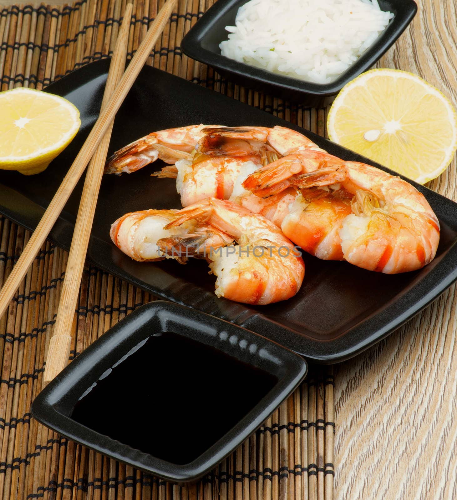 Delicious Asian Style Roasted Shrimps with Soy Sauce, Boiled Rice, Lemon and Chopsticks on Straw Mat background closeup