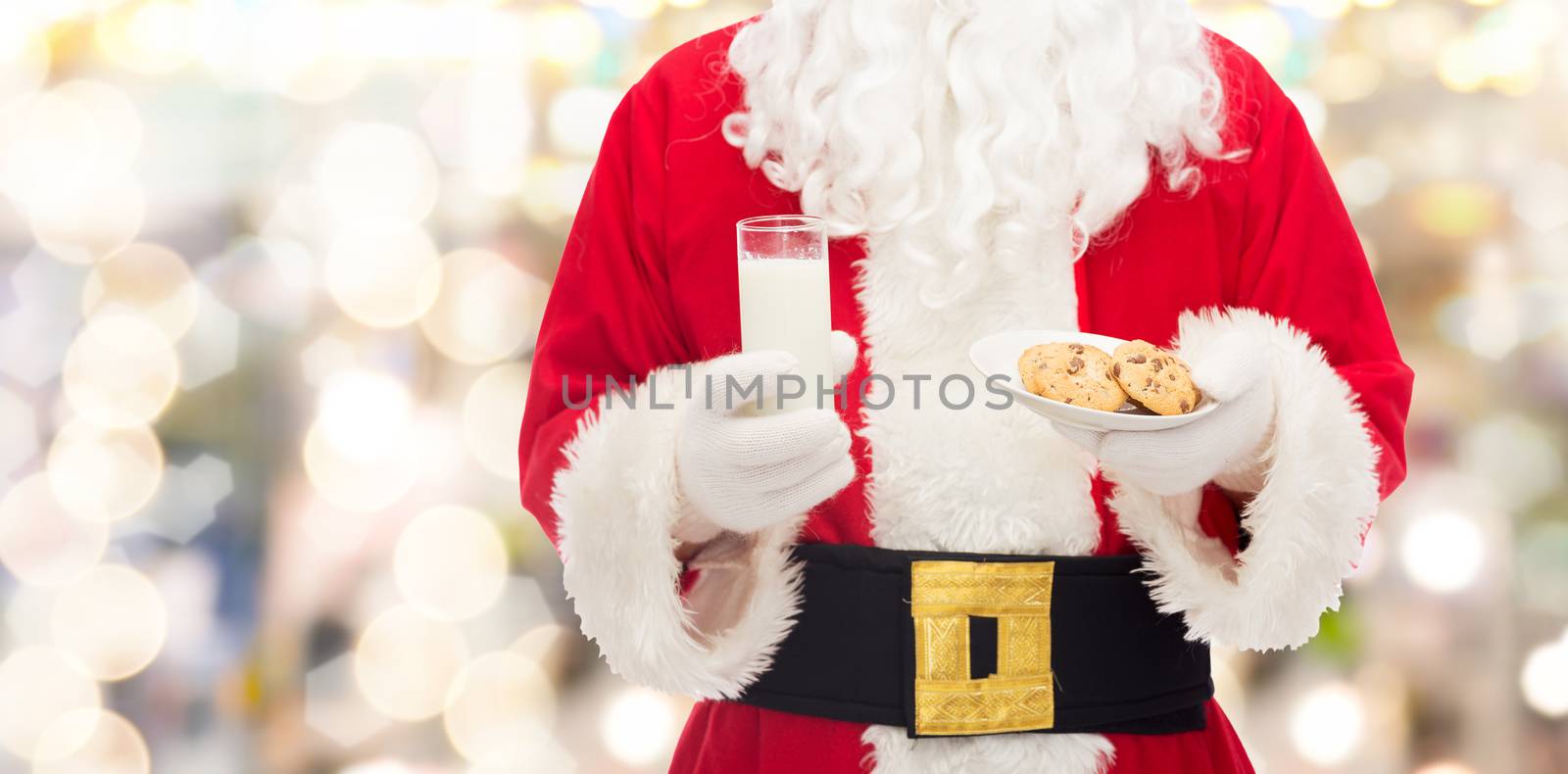 christmas, holidays, food, drink and people concept -close up of santa claus with glass of milk and cookies over lights background