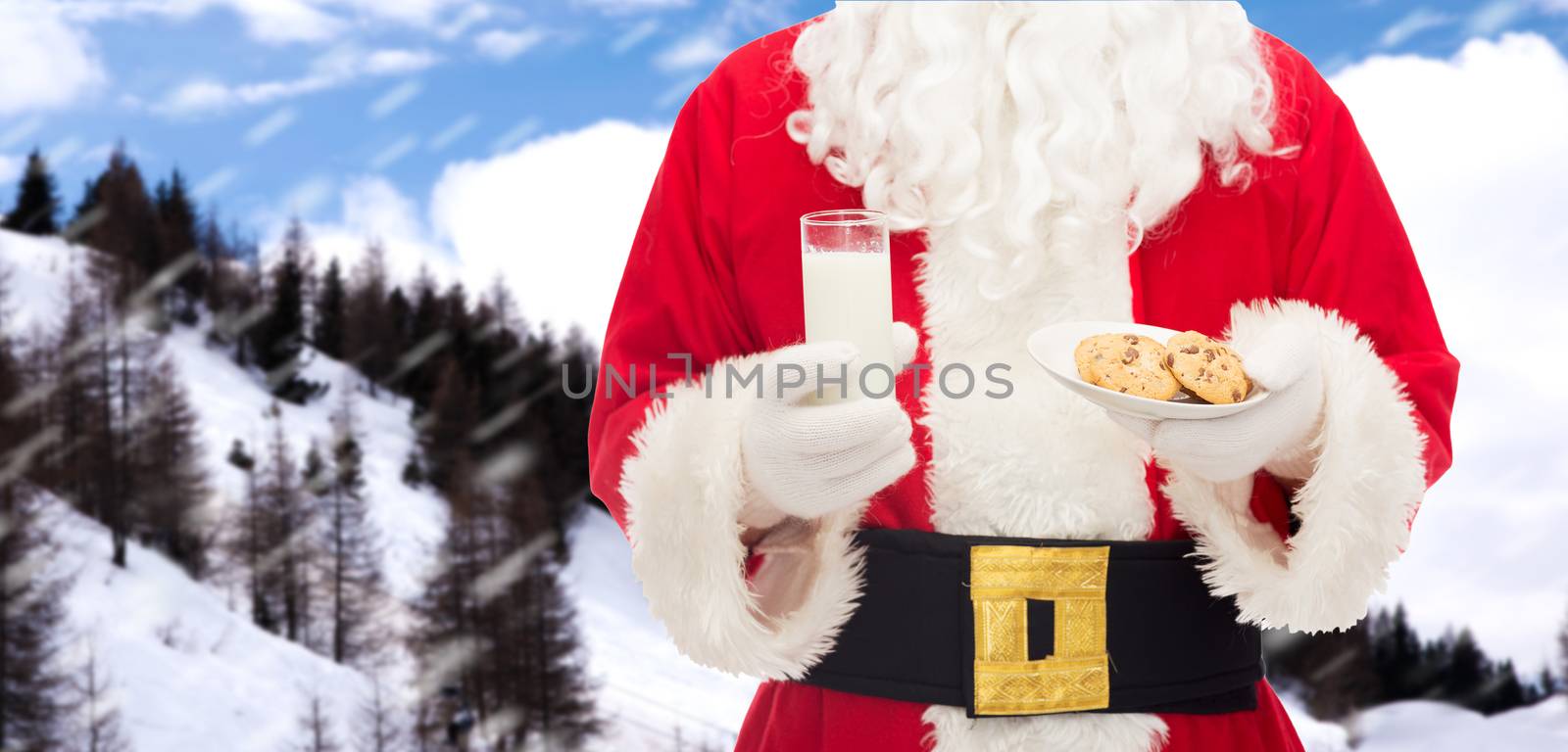 christmas, holidays, food, drink and people concept - close up of santa claus with glass of milk and cookies over snowy mountains