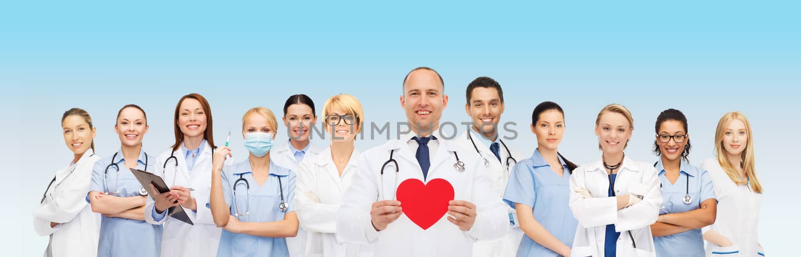 medicine, profession, teamwork and healthcare concept - international group of smiling medics or doctors with clipboard and stethoscopes holding red paper heart shape over blue background