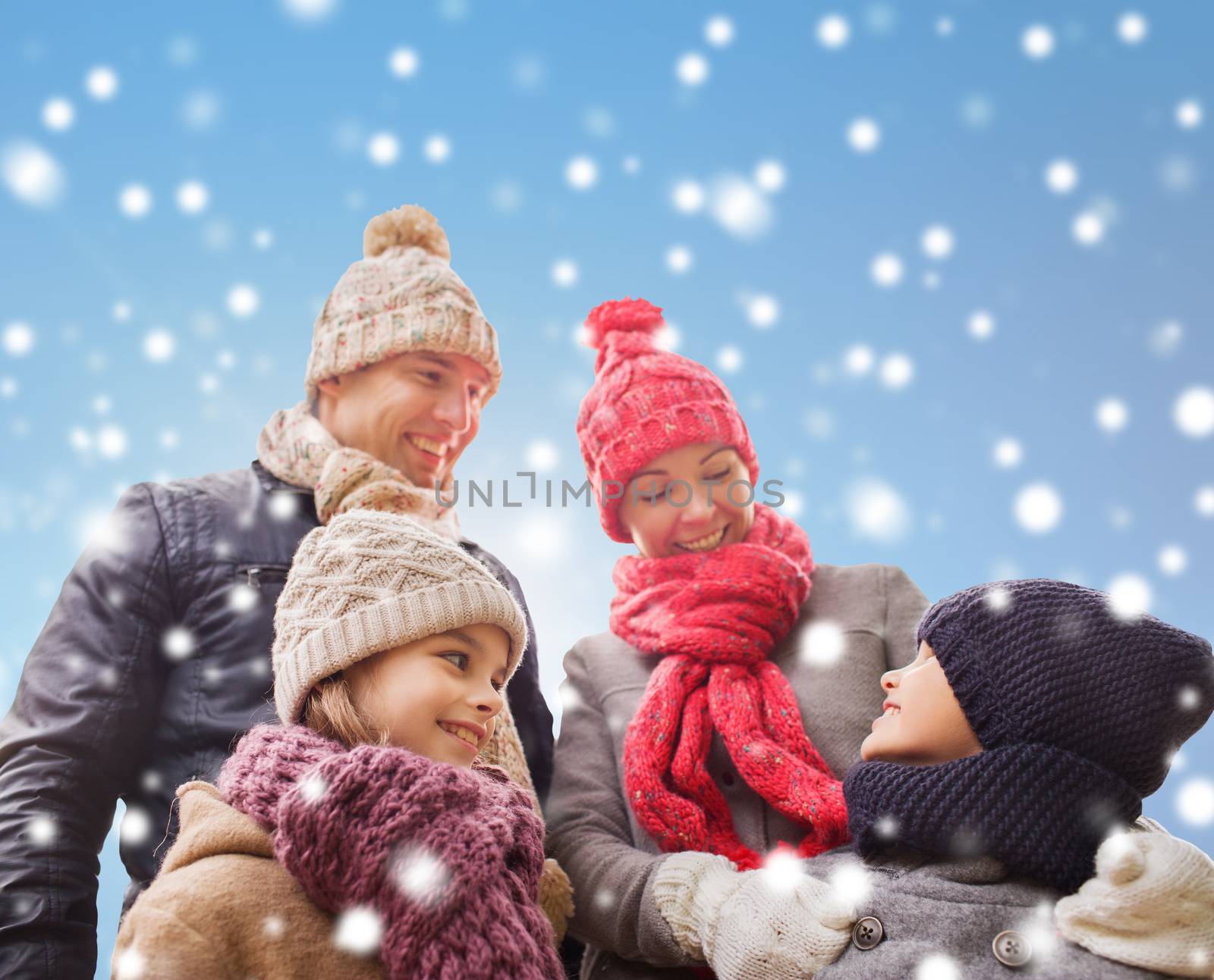 family, childhood, season and people concept - happy family in winter clothes over blue snowy background