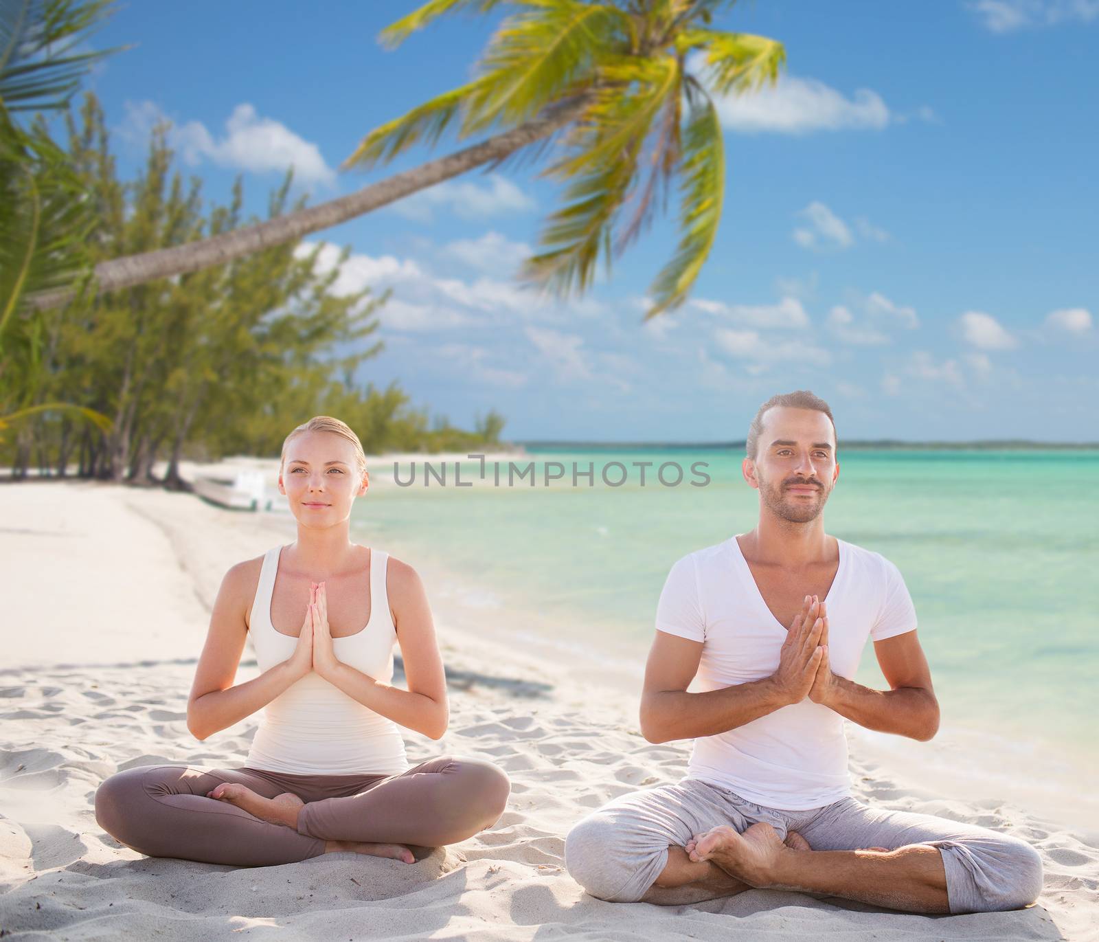 sport, yoga, people, travel and lifestyle concept - smiling couple meditating sitting on tropical beach