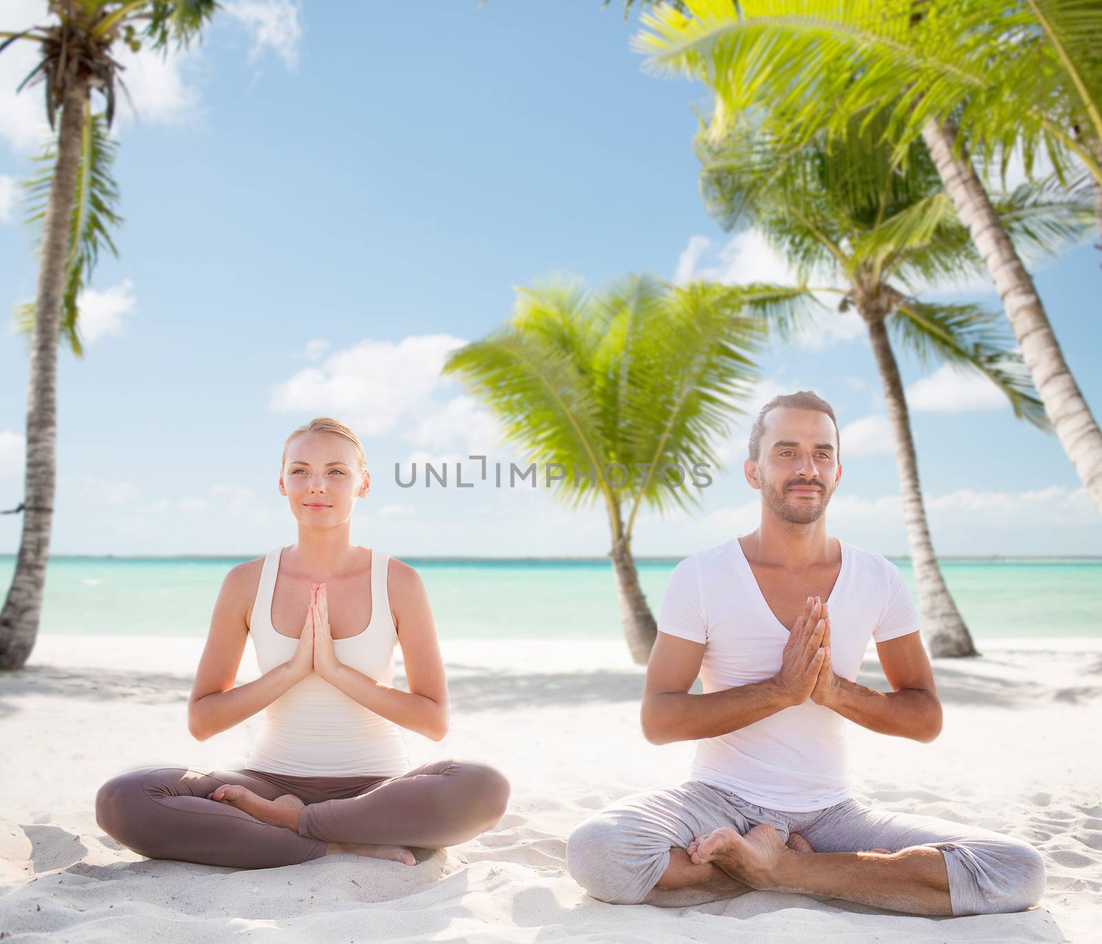 sport, yoga, people, travel and lifestyle concept - smiling couple meditating sitting on tropical beach