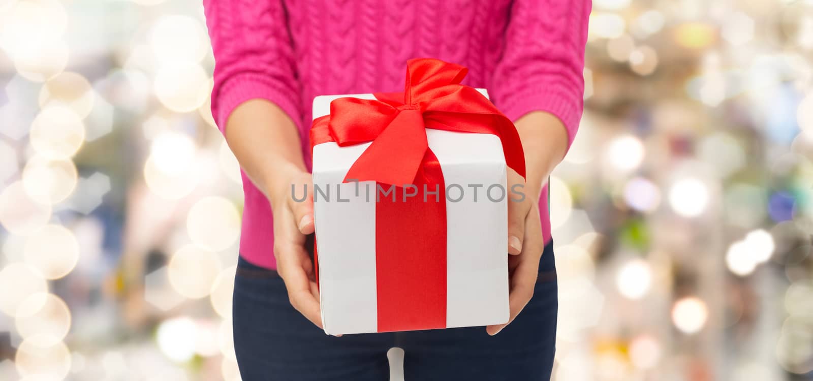 christmas, holidays and people concept - close up of woman in pink sweater holding gift box over lights background