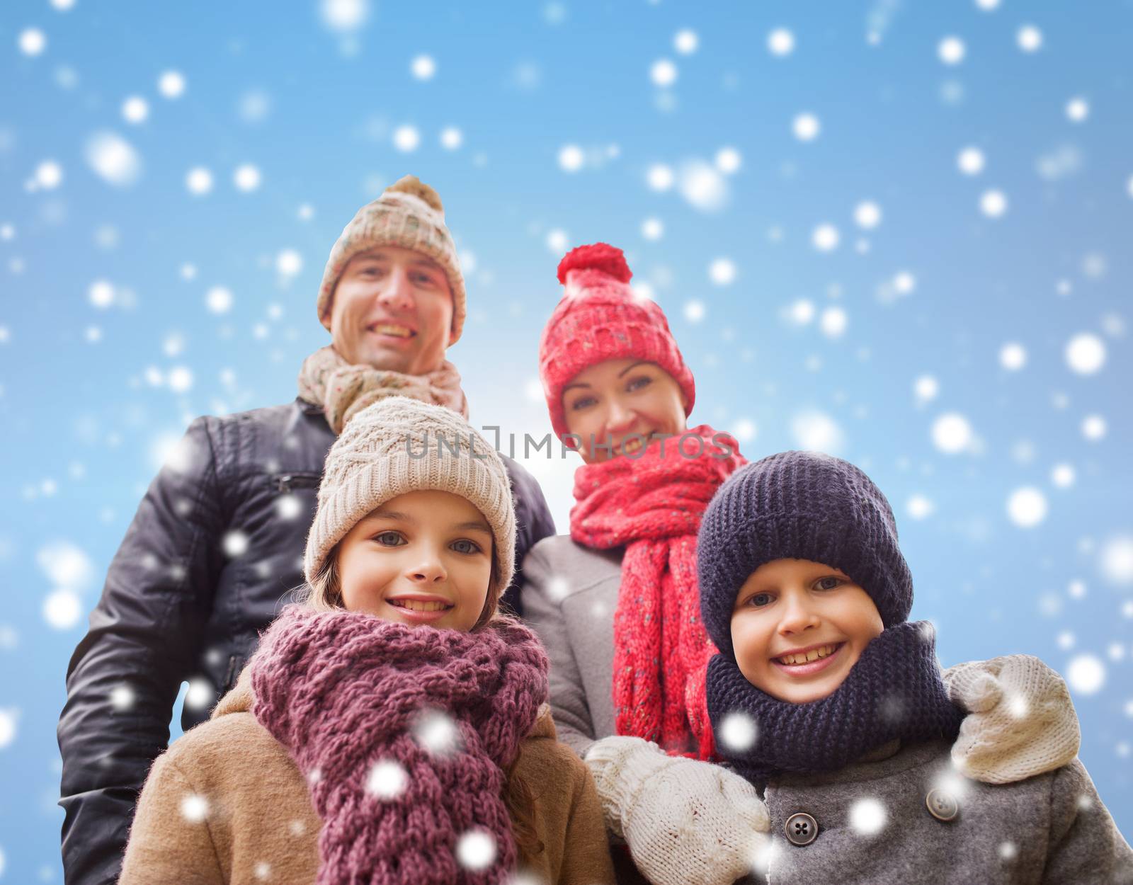 family, childhood, season and people concept - happy family in winter clothes over blue snowy background