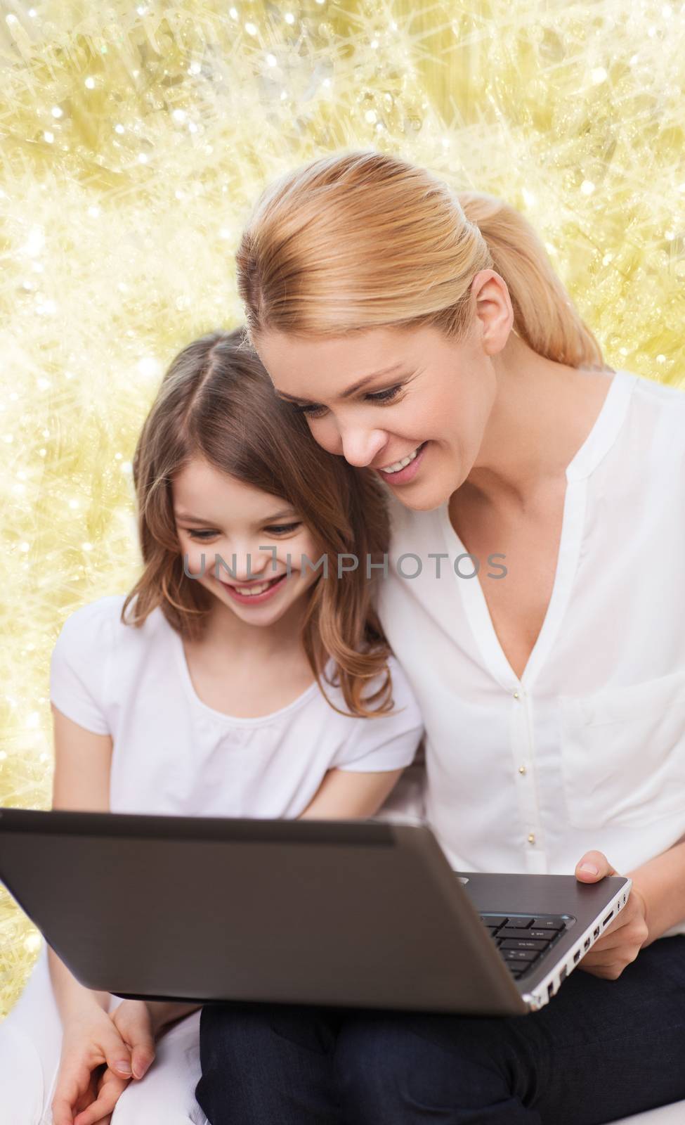 family, childhood, holidays, technology and people concept - smiling mother and little girl with laptop computer over yellow lights background