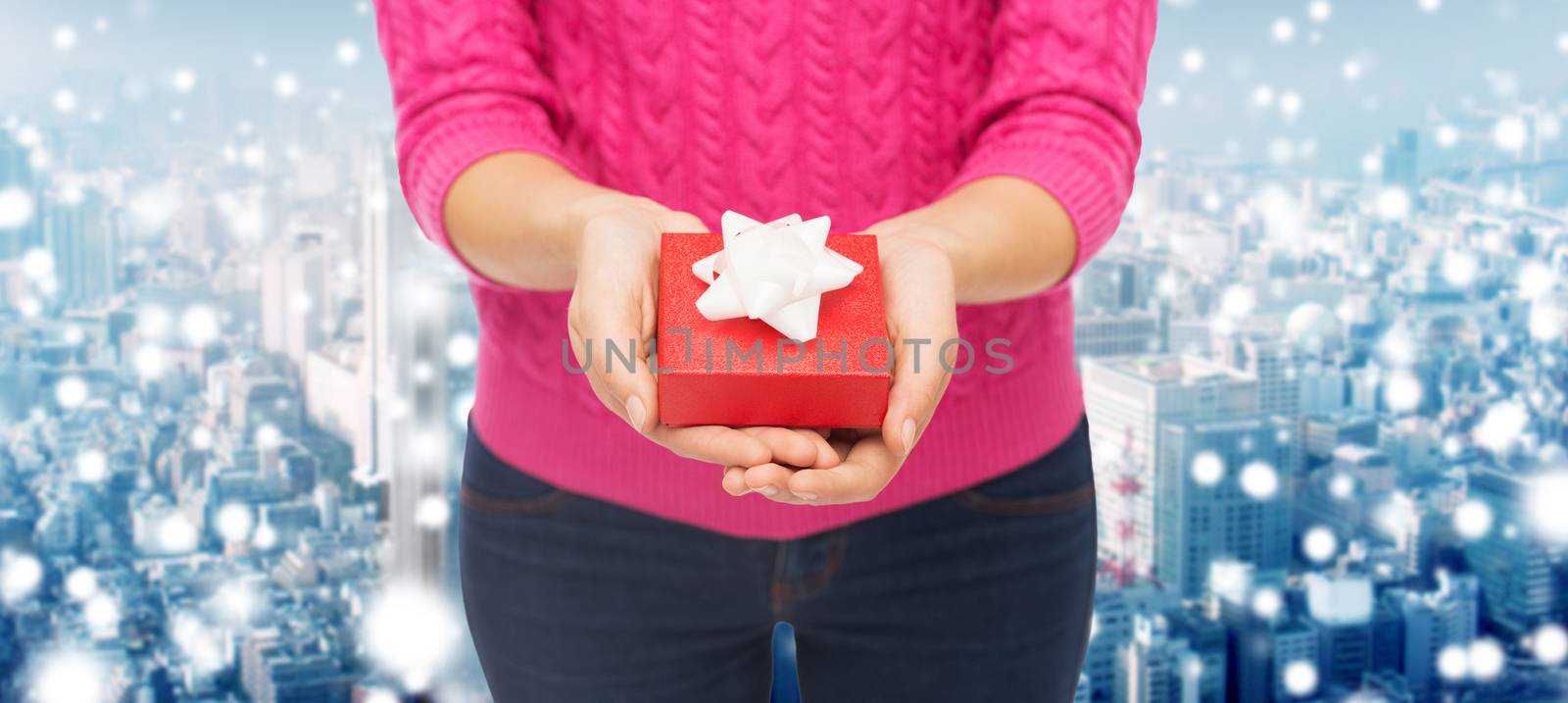 christmas, holidays and people concept - close up of woman in pink sweater holding gift box over snowy city background