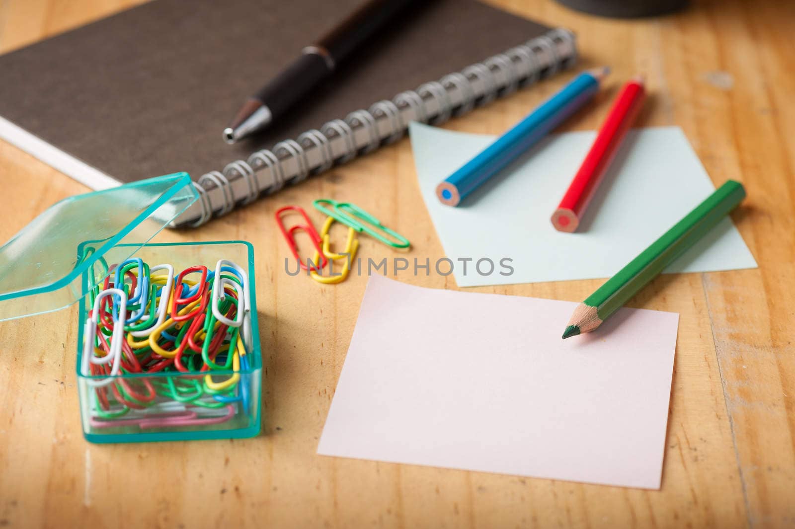 Notebook and sticky paper, paper clip, color pencil, and pen on wood table