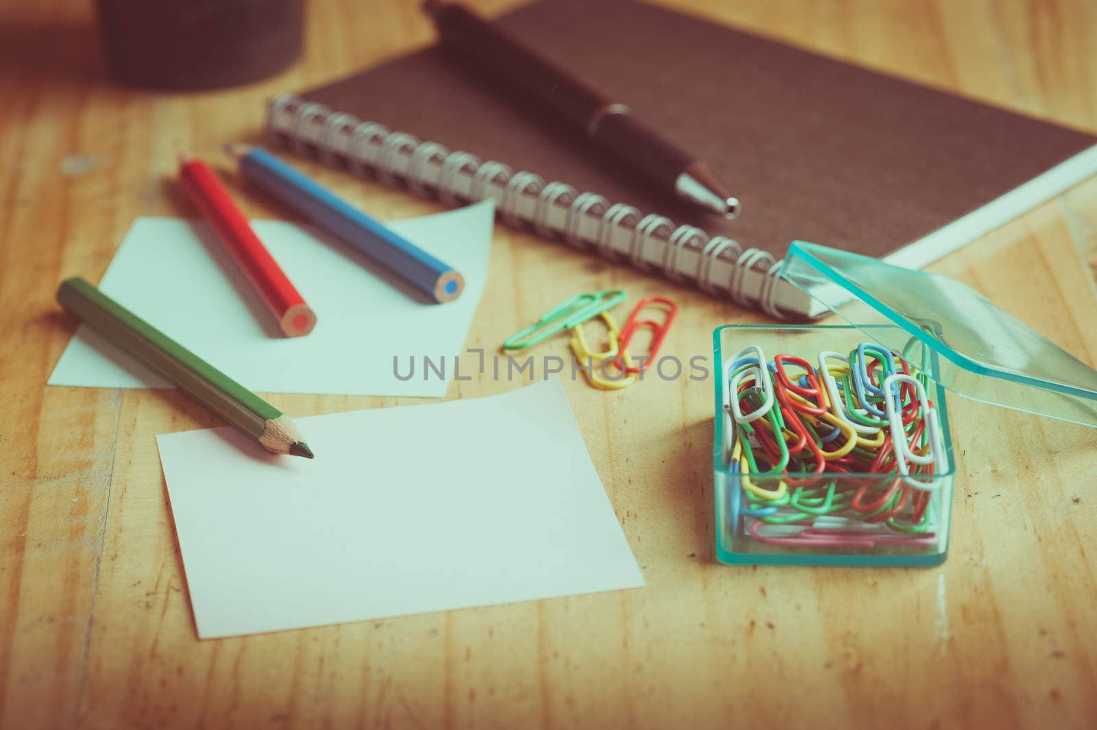 Notebook and sticky paper, paper clip, color pencil, and pen on wood table with vintage filter effect