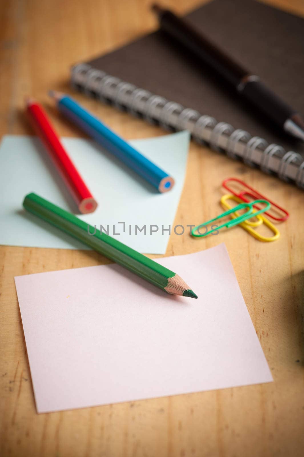 Notebook and sticky paper, paper clip, color pencil, and pen on wood table