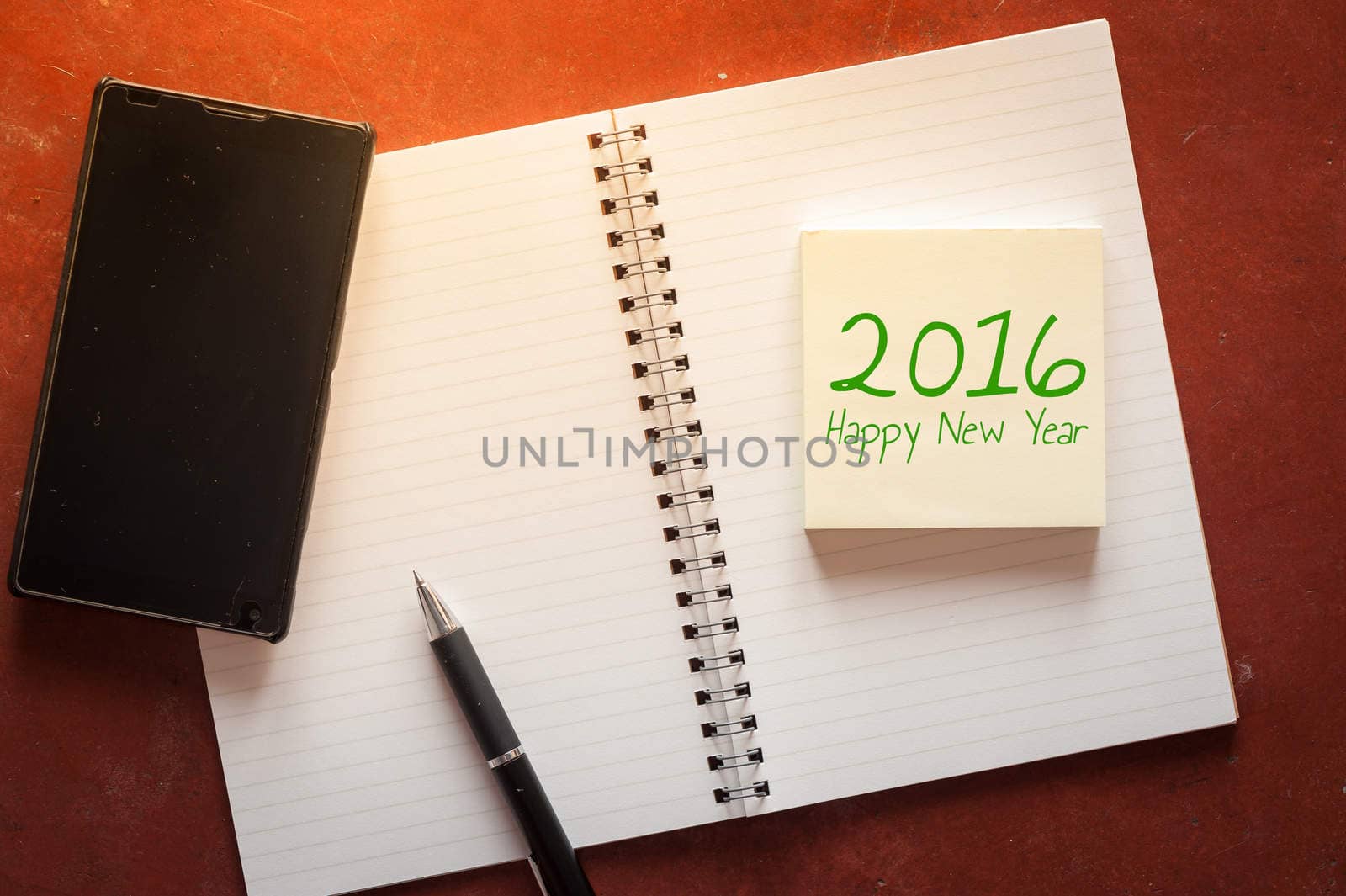 "2016 Happy new year" is written on opened notepad with pen, small sticky paper and black smart phone on rustic cement background with low key scene.
