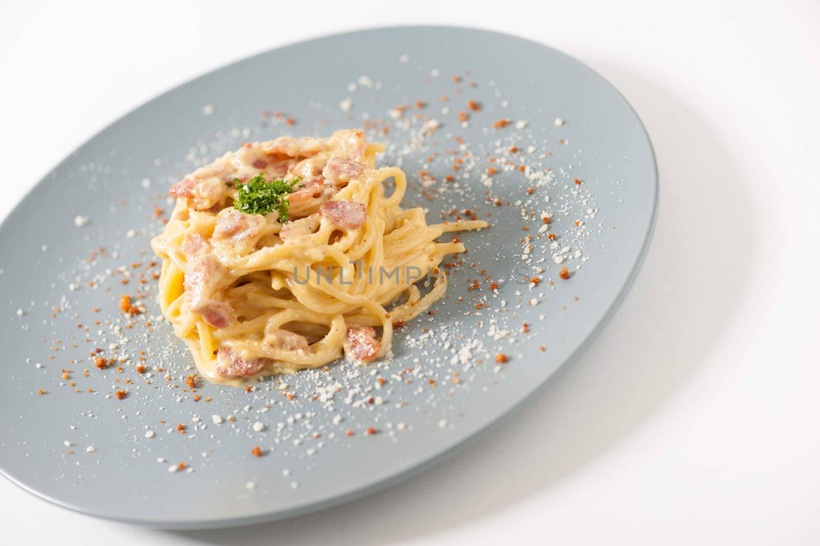 Carbonara pasta with bacon in grey ceramic dish.