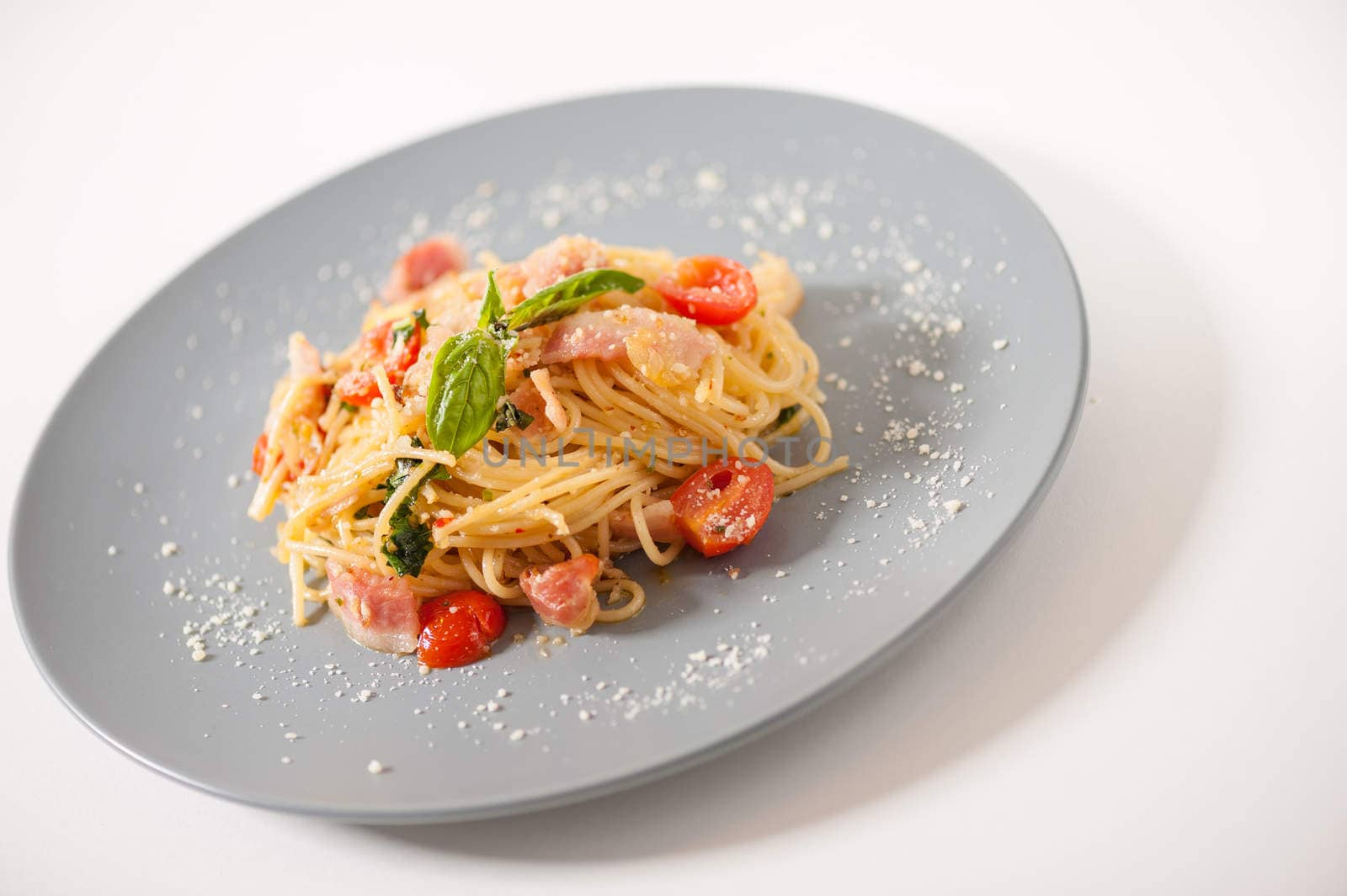 Pasta with bacon and tomato in grey ceramic dish.