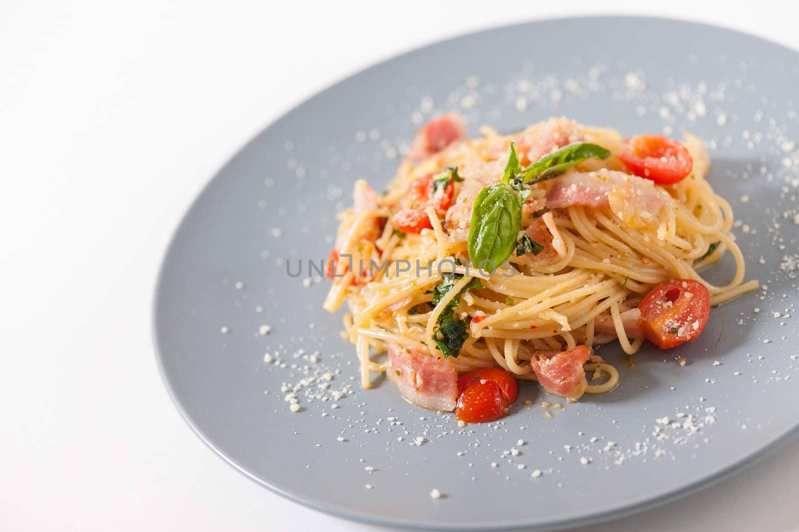 Pasta with bacon and tomato in grey ceramic dish.