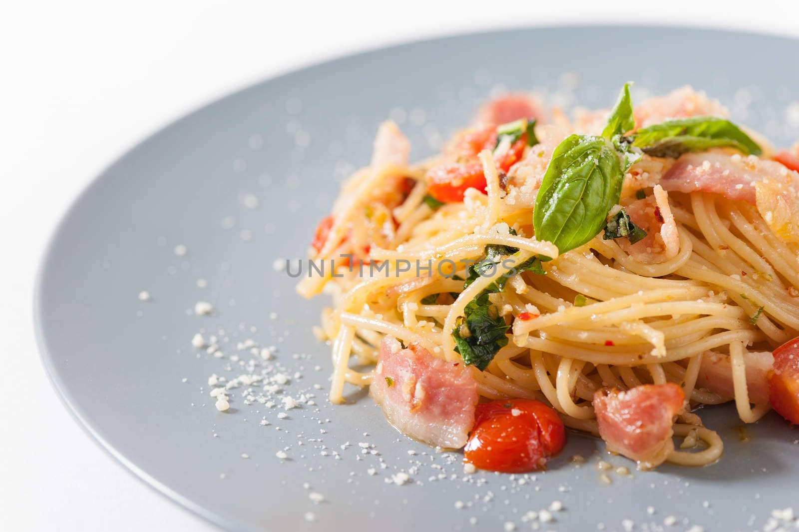 Pasta with bacon and tomato in grey ceramic dish.
