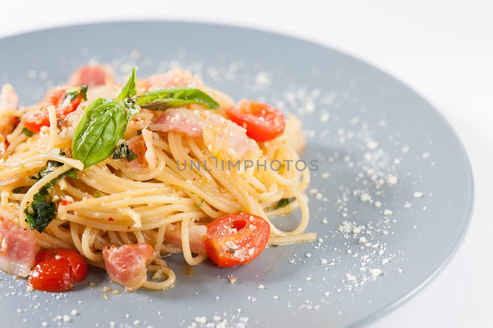 Pasta with bacon and tomato in grey ceramic dish.