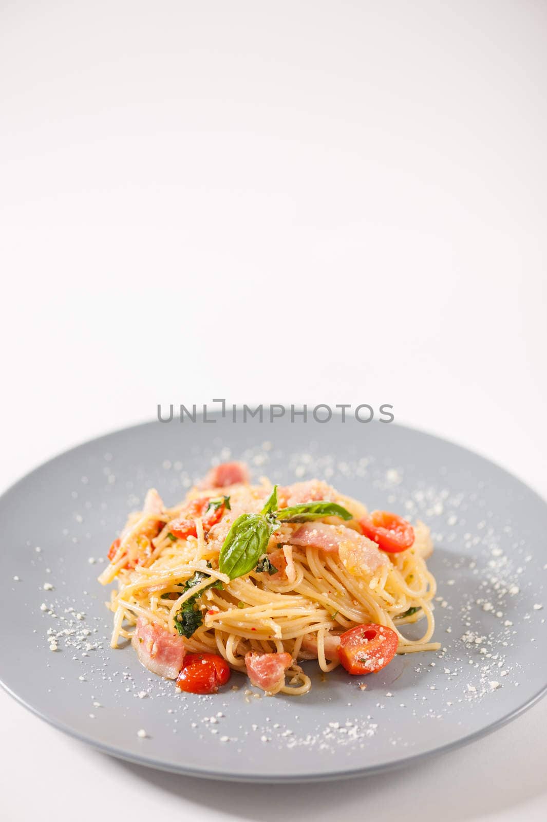 Pasta with bacon and tomato in grey ceramic dish.