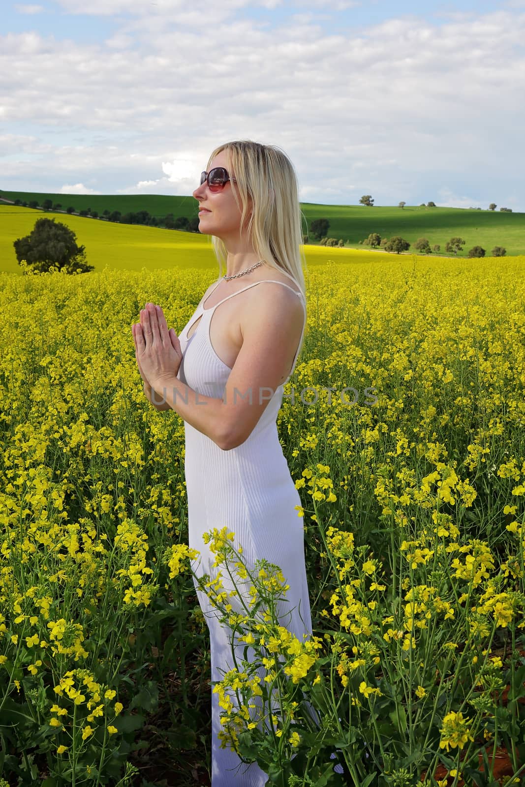 Woman praying to God or mother earth for rain or abundant harvest or she could ve meditating among nature etc.  Standing in a field of golden canola and wearing a pure white dress
