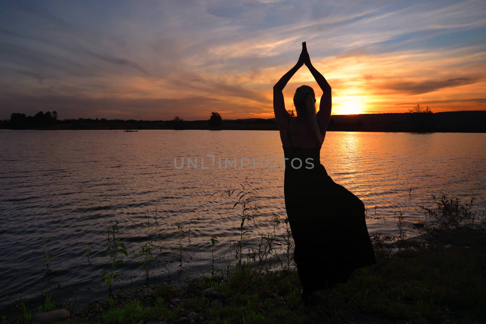 Woman relaxing and meditating yoga as the sun goes down.  Silhouette of woman doing Tree pose Vrksasana