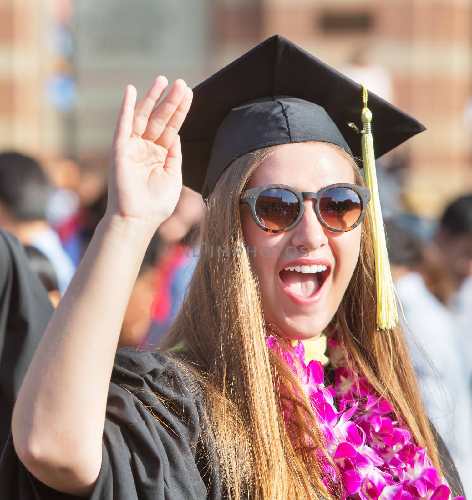 Excited female college graduate in sunglasses waving hand