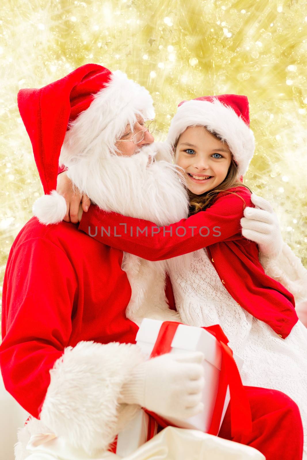 holidays, christmas, childhood and people concept - smiling little girl hugging with santa claus over yellow lights background
