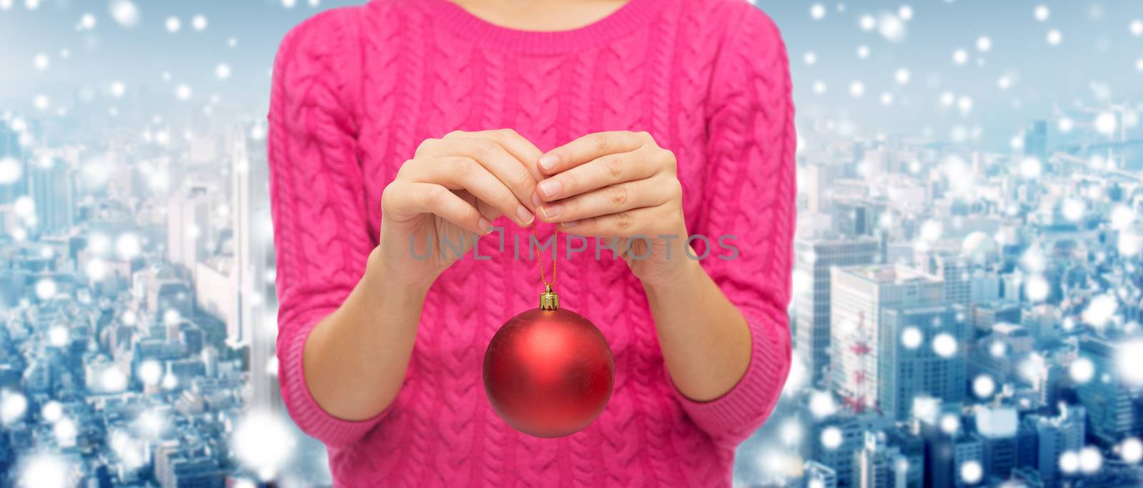 christmas, decoration, holidays and people concept - close up of woman in pink sweater holding christmas ball over snowy city background