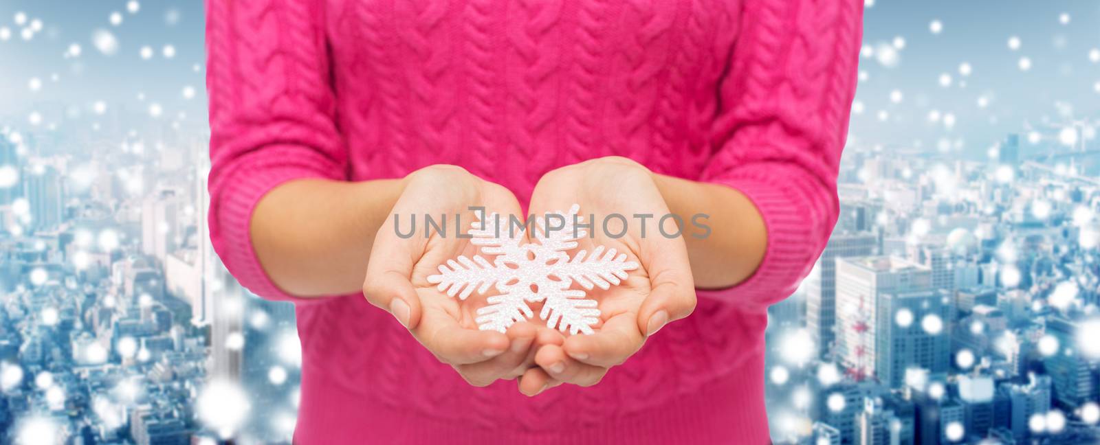 christmas, holidays and people concept - close up of woman in pink sweater holding snowflake over snowy city background