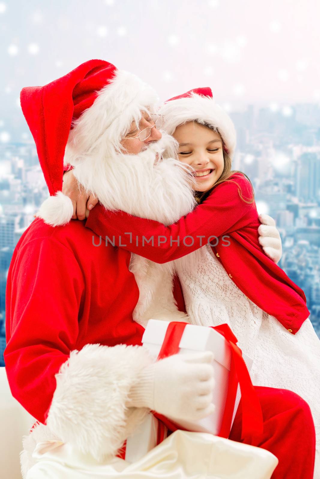 holidays, christmas, childhood and people concept - smiling little girl hugging with santa claus over snowy city background