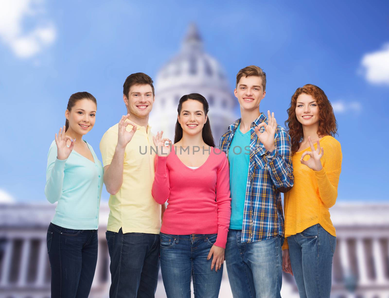friendship, tourism, travel and people concept - group of smiling teenagers showing ok sign over white house background